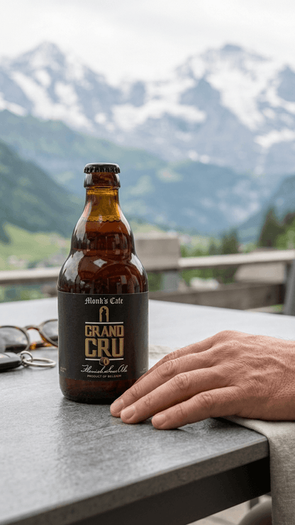 Flasche Grand Cru Monk's Café 33cl Bier auf grauem Tisch mit Bergpanorama im Hintergrund.