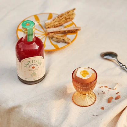 Flaschenminiatur roter Jardins-Aperitif mit Glas und knusprigen Brotscheiben auf weißer Tischdecke.